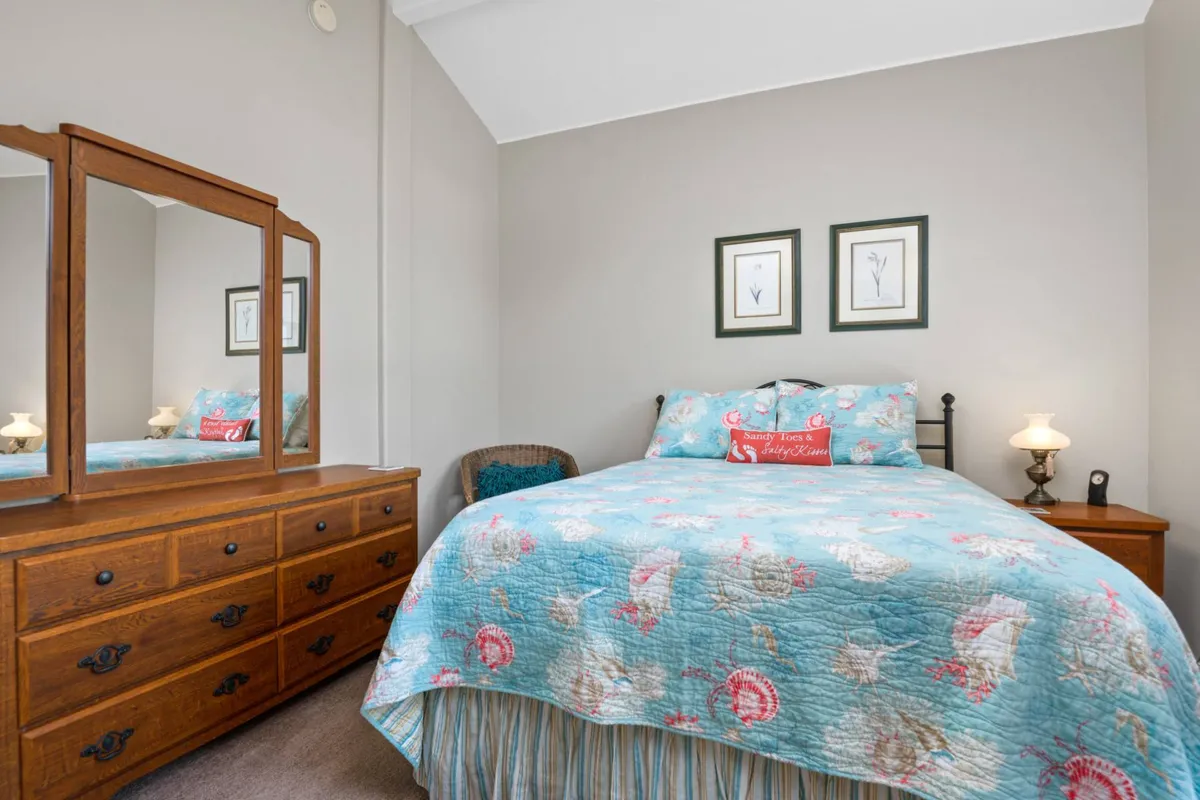 A welcoming bedroom with a comfortable bed, a dresser, a mirror, a lamp, and framed art on the wall. Soft natural light gives the space a tranquil, peaceful ambiance, ideal for unwinding and enjoying personal moments of relaxation.