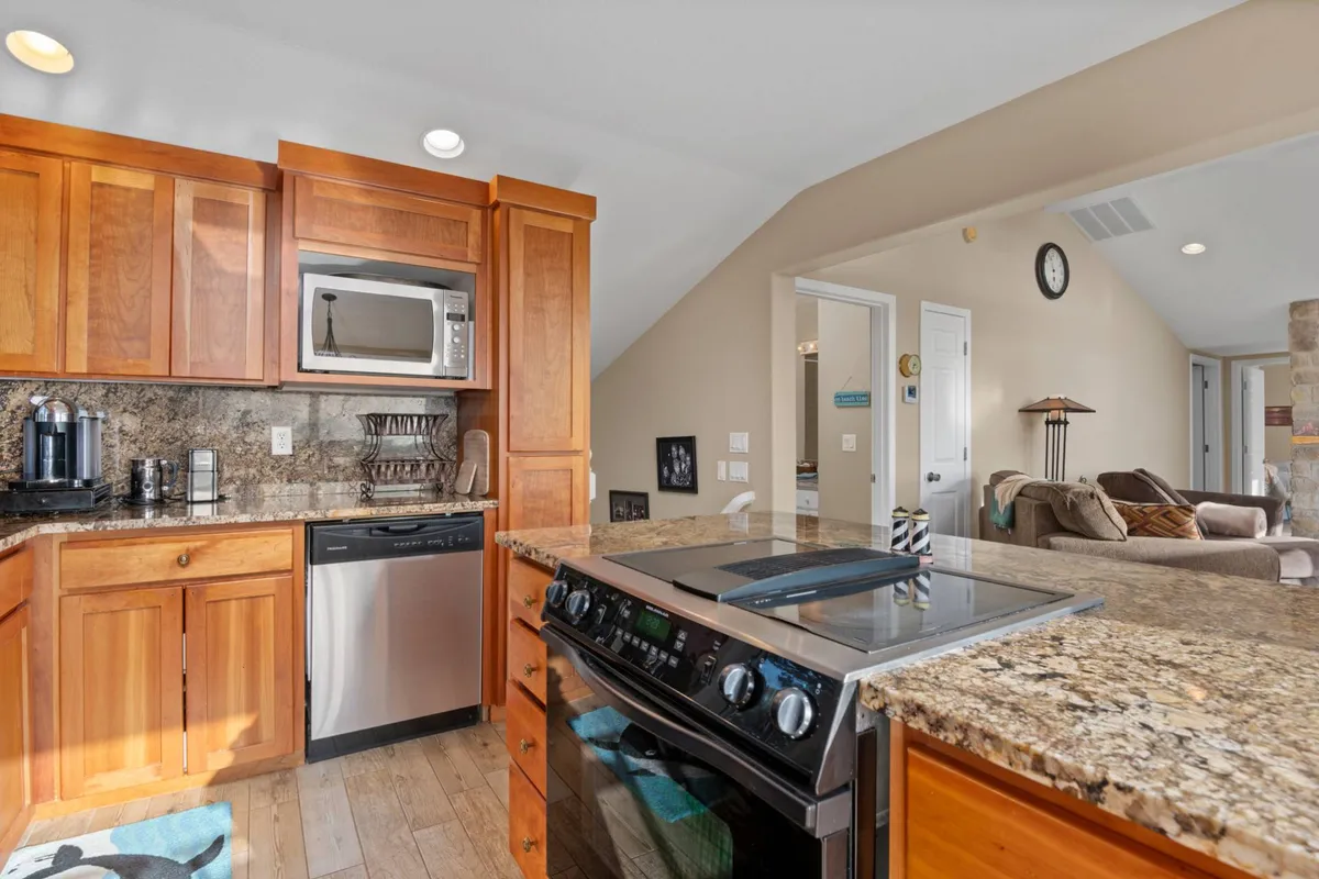 A modern kitchen with shining granite countertops, wood cabinetry, and stainless steel appliances. The open layout connects seamlessly to adjacent living spaces, hinting at easy flow for entertaining and shared meals.