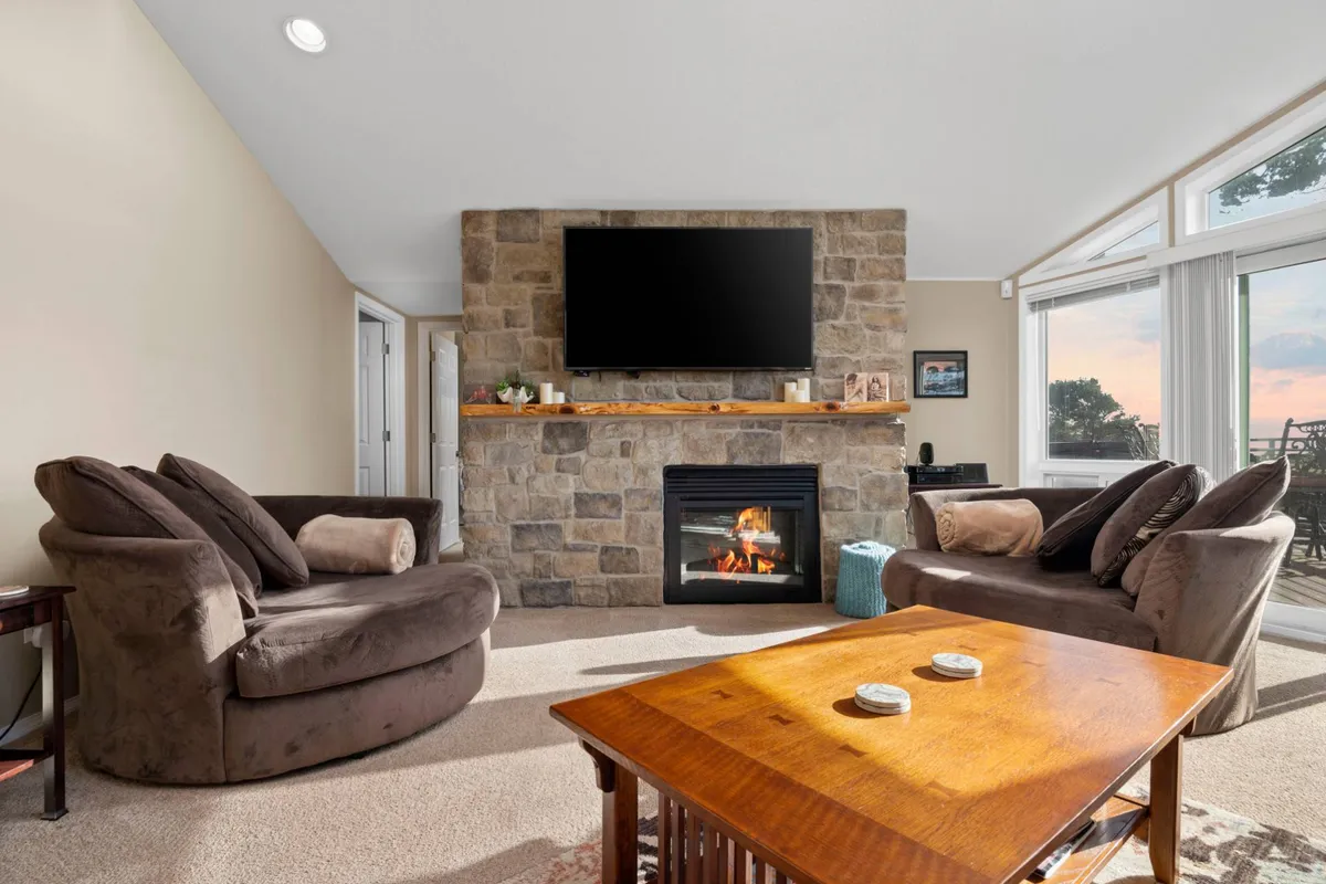 A warm, open-concept living area with a stone fireplace, comfortable seating, wooden coffee table, and large windows revealing the view outside. The layout is inviting and perfect for relaxing movie nights or long conversations, echoing the section's focus on comfort and togetherness.