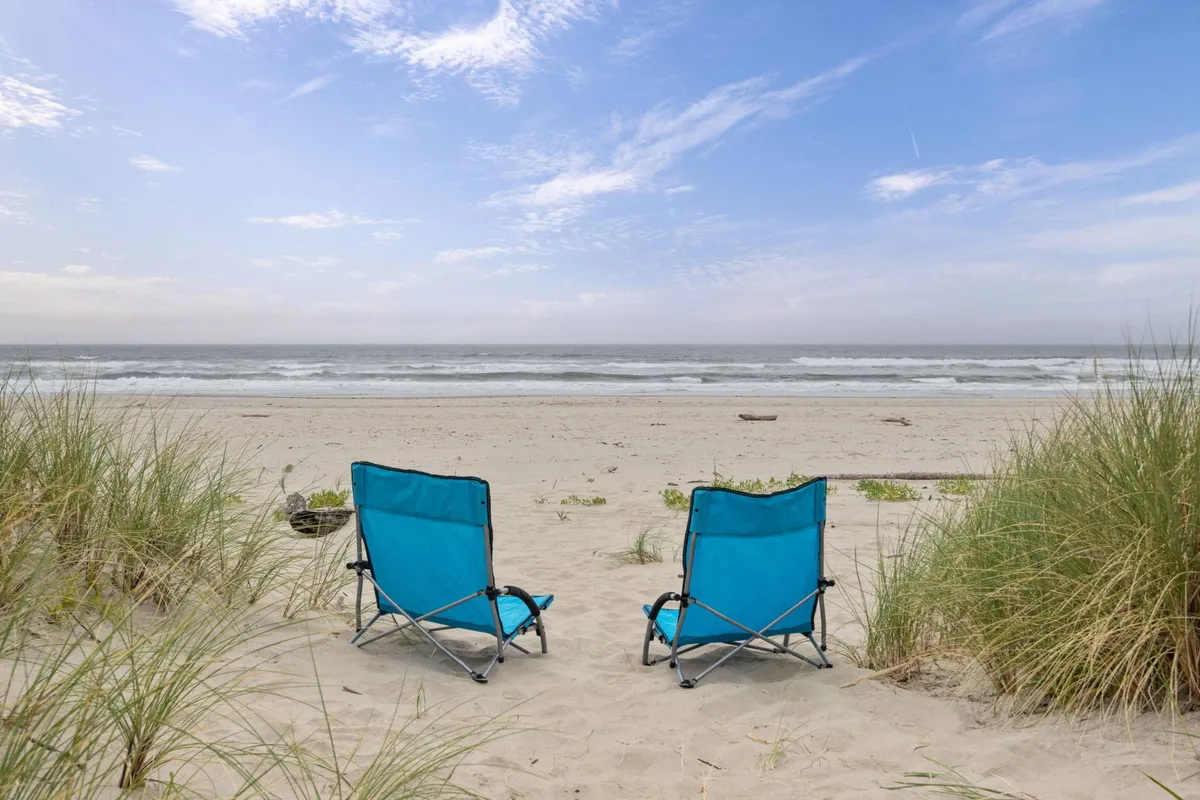 A peaceful deck setup with blue beach chairs facing a stunning ocean view, bordered by dune grass. The environment invites you to relax, sunbathe, or birdwatch while immersed in coastal beauty.
