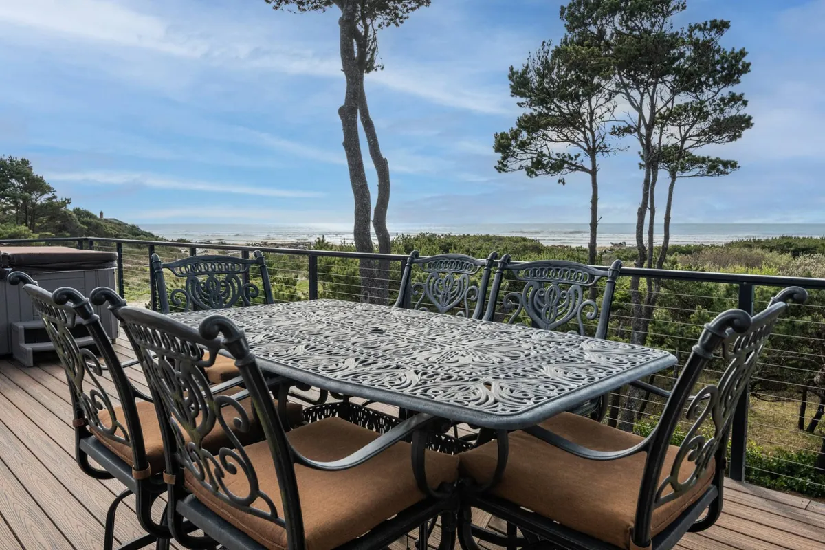 An outdoor dining area set with an ornate table overlooks the ocean, framed by surrounding trees. The setting feels tranquil and perfectly suited for enjoying both morning coffee and evening sunsets while immersed in nature.