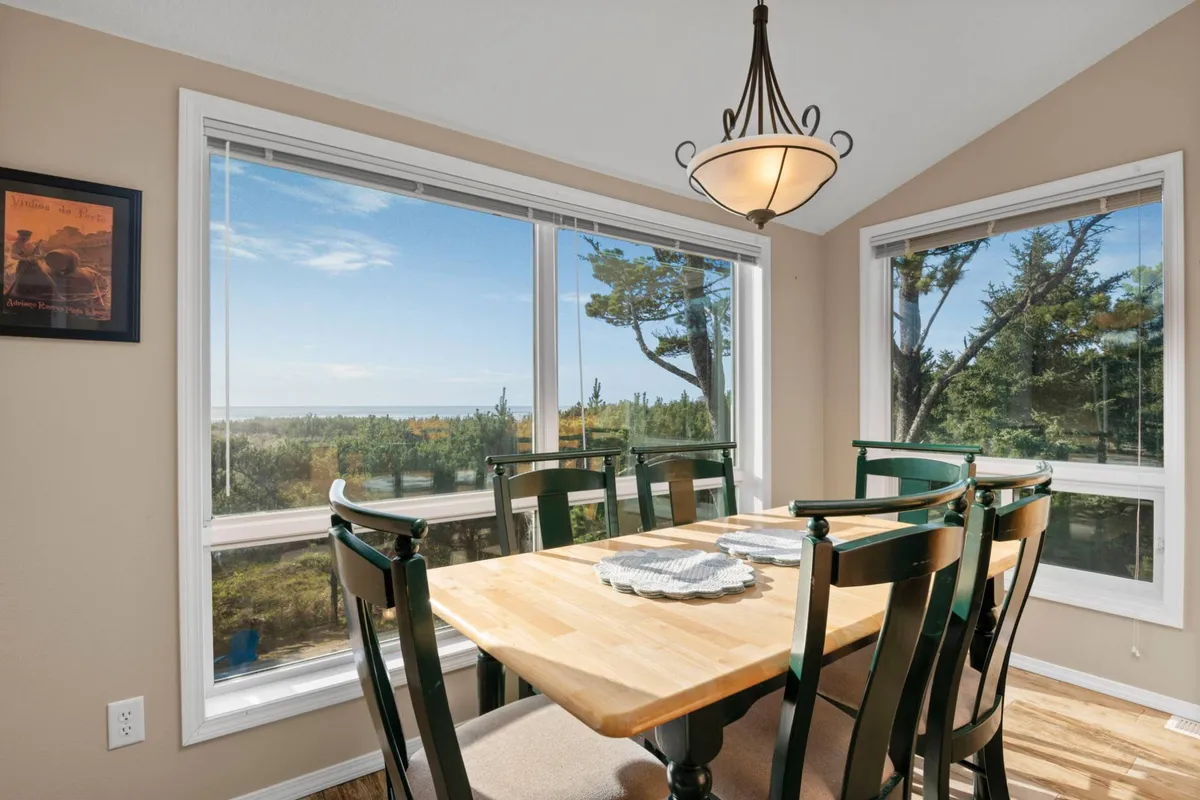 A dining area featuring a large table under a stylish chandelier, positioned next to expansive windows with breathtaking ocean views. The setup is warm and inviting, ideal for family meals and celebratory gatherings.