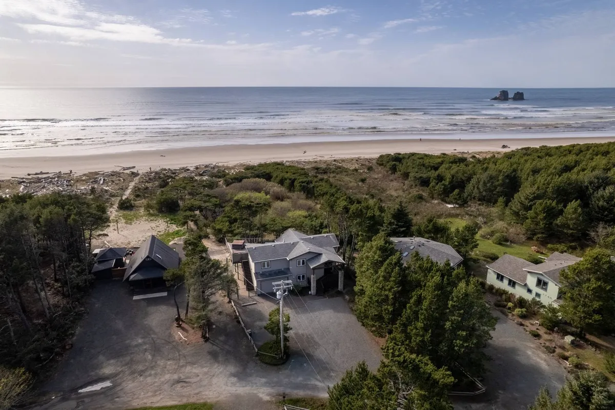 This image showcases the house with direct beach access, the beachfront view, surrounding trees, and the proximity to the water. The inviting scene hints at activities like beachcombing, building sandcastles, and enjoying the Pacific views, all just steps from the private deck.