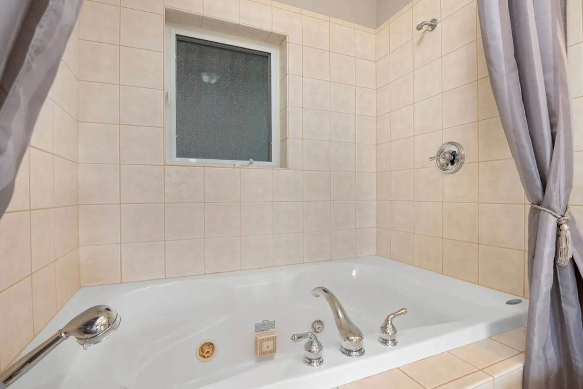 A serene bathroom featuring a spacious jacuzzi tub with a shower fixture and a window that lets in soft natural light. The clean lines and inviting setup evoke a spa-like experience, perfect for unwinding after a long day.