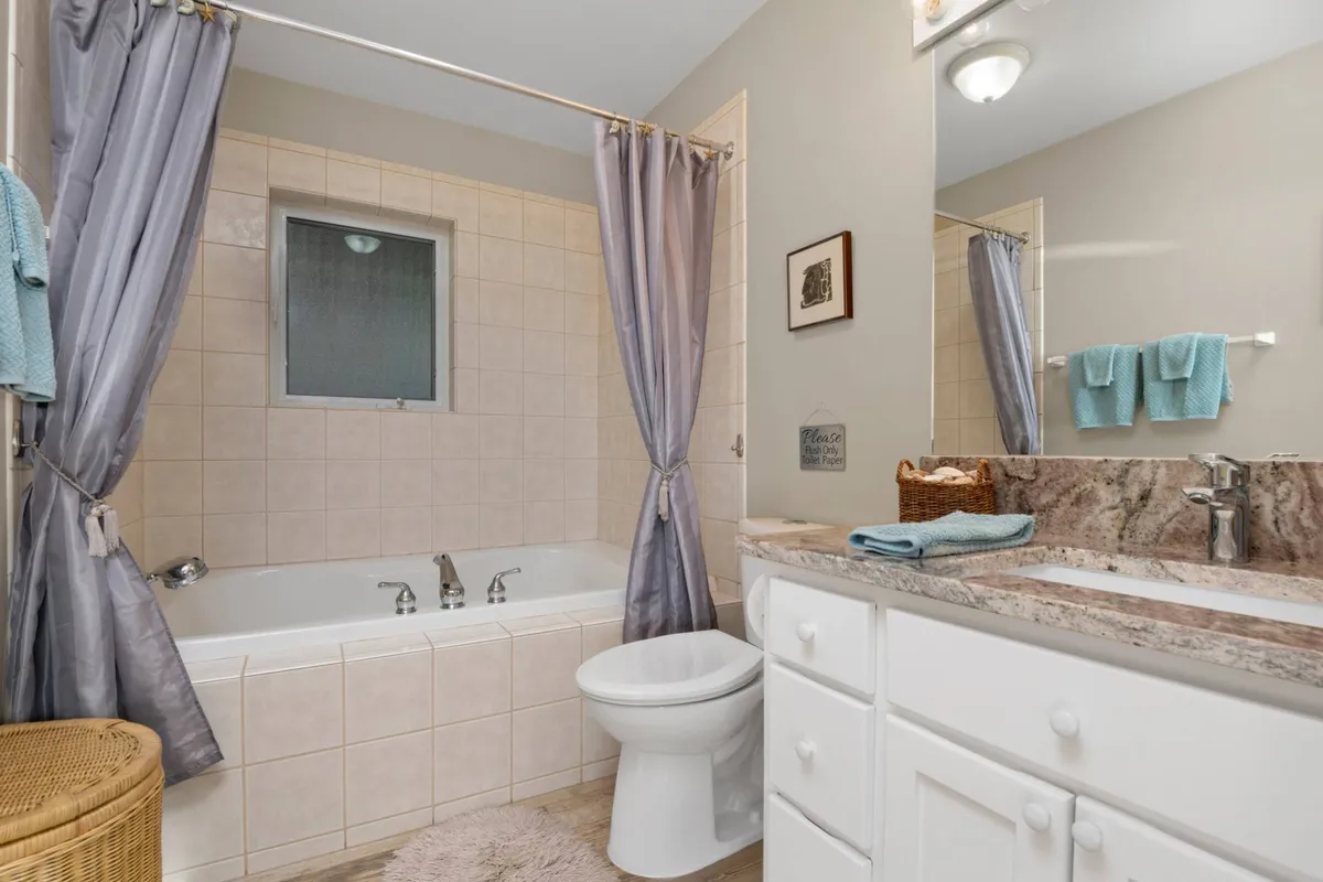 A tranquil bathroom scene with a bathtub, sink and mirror, shower curtain, and neatly arranged towels. The space feels fresh and inviting, with a relaxing atmosphere perfect for washing off after a day at the beach or preparing for the day ahead.